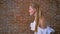 Young caucasian blonde in a white blouse funny dancing, brick wall in background