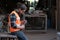 Young caucasian carpenter in a uniform. Wearing protective glasses and sitting in front of the factory during the woodwork, he