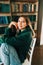 Young caucasian cheerful woman student sitting in a white chair near bookshelf in library