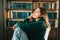 Young caucasian cheerful woman student sitting in a white chair near bookshelf in library