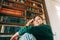 Young caucasian cheerful woman student sitting in a white chair near bookshelf in library