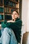 Young caucasian cheerful woman student sitting in a white chair near bookshelf in library