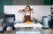 Young caucasian coffee shop staff  dressed in brown apron holding coffee drink in plastic cup with both hands. Morning atmosphere