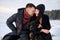 Young caucasian couple in love sitting on stone with dog on winter beach, embracing, enjoy the romantic moment, feeling intimacy
