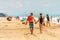 Young Caucasian couple walk on sand of sunny Black Sea Blaga beach resort drinking bear with people on background