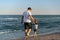 Young Caucasian dad with little son walk warm summer day along the sea coast. Summer family vacation concept. Friendship father
