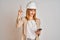 Young caucasian engineer woman using smartphone and wearing safety helmet surprised with an idea or question pointing finger with