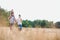 Young Caucasian family walking across field with young child on her fathers shoulders with the wife holding a bouquet of flowers