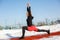 Young caucasian female blonde in red leggings stretching exercise on a red running track in a snowy stadium. fit and sports
