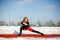 Young caucasian female blonde in red leggings stretching exercise on a red running track in a snowy stadium. fit and sports