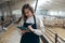 Young Caucasian Female Farm Owner with Tablet in large Livestock Stall with white Dairy Goats