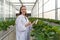 Young caucasian female fruit researcher in white gown holding Urea in PET preform bottle while working in indoor strawberries farm