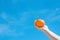 Young Caucasian Female Hand Holding Whole Ripe Orange on Blue Sky Background. Summer Vacation Wanderlust Traveling