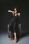 Young Caucasian female model posing in studio black background.Girl sitting in a black dress on a dark wall. Subject