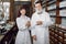 Young Caucasian female pharmacist and her senior bearded man colleague, standing together with medicines packages near