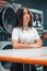 Young Caucasian female standing in front of laundry machines, vertical shot