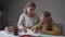 Young Caucasian female tutor explaining mistakes to the cute little girl. Schoolchild writing in the exercise book