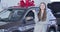 Young Caucasian girl bragging car keys next to new vehicle with big red bow in dealership. Happy successful