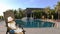 Young caucasian girl sitting on armchair and reading book. Swimming pool and palm trees at background. Have same clip