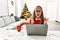 Young caucasian girl sitting on the table working using laptop by christmas tree crazy and mad shouting and yelling with