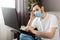 Young caucasian gloomy man in stress working from home office wearing protective mask using laptop and internet. Coronavirus covid