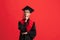 Young caucasian guy, student, graduate in mantle and mortarboard isolated over red studio background.