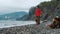 Young Caucasian guy walks along pebbly seashore with Australian and German Shepherd dogs. Male Owner and pets on