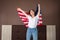 A young caucasian happy woman waves an American flag. Indoor. The concept of the American national holidays and