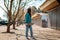 A young Caucasian hipster woman walks down the street with a skateboard in her hands and turns back. In the background, an alley.