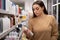 Young caucasian lady with a trolley and long hair in a supermarket chooses shampoo. A woman buys groceries and basic goods at a