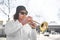 Young caucasian long-haired man in shirt and sunglasses playing trumpet outdoor