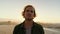 A young Caucasian male with curly hair staring into camera on the beach during sunset. Male looking serious. High