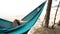 Young caucasian male resting lying on blue hammock outdoors near lake.