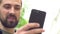 A young caucasian man with a beard holds a phone on his hand and talks. The blogger communicates by video call. The guy smiles on