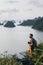 Young Caucasian man with a camera standing on a cliff overlooking Halong Bay during sunset, Vietnam