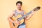 Young caucasian man with curly hair playing classical guitar smiling with a happy and cool smile on face