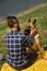 Young Caucasian man with dreadlocks is resting in park with dog. Male owner strokes German Shepherd sitting on yellow blanket in