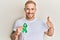 Young caucasian man holding support green ribbon smiling happy and positive, thumb up doing excellent and approval sign