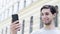 A young caucasian man holds a phone on his hand and communicates by video call. Blogger guy sincerely smiles on camera