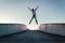 Young caucasian man in jeans and hoodie jumping with spread out arms on concrete bridge. Mid air parkour pose in city environment