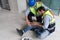 Young caucasian man in safety vest gripped his knee and screams in pain. Due to injuries at the construction site. His asian