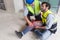 Young caucasian man in safety vest gripped his knee and screams in pain. Due to injuries at the construction site. His asian