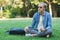 Young caucasian man sitting on the grass of a green park and holding a coffee thermos