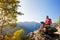 Young caucasian man sitting outdoor on a rock working on a laptop pc in mountain area.