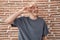 Young caucasian man standing over bricks wall doing peace symbol with fingers over face, smiling cheerful showing victory