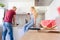 Young caucasian man washing up dishes, while his girlfriend who is sitting on kitchen counter, holds glass of red wine