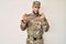 Young caucasian man wearing camouflage army uniform doing money gesture with hands, asking for salary payment, millionaire