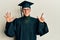 Young caucasian man wearing graduation cap and ceremony robe showing and pointing up with fingers number seven while smiling