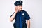 Young caucasian man wearing police uniform smiling with hand over ear listening an hearing to rumor or gossip