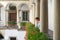 Young caucasian shorthair woman dressed in blue dress smiling while walking in italian courtyard